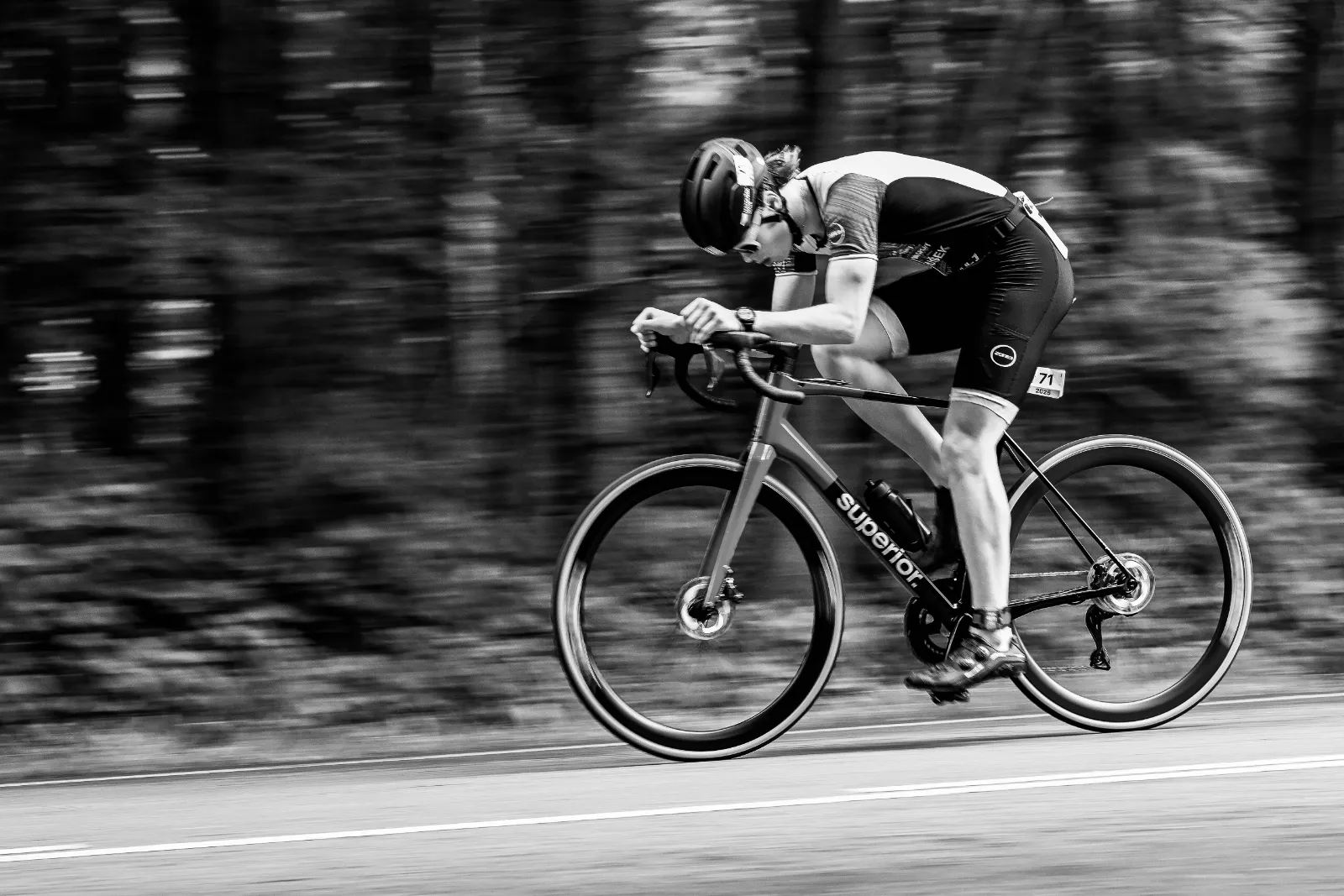 Oliver on a road bike, low in an aero position, panning shot. Black and white.