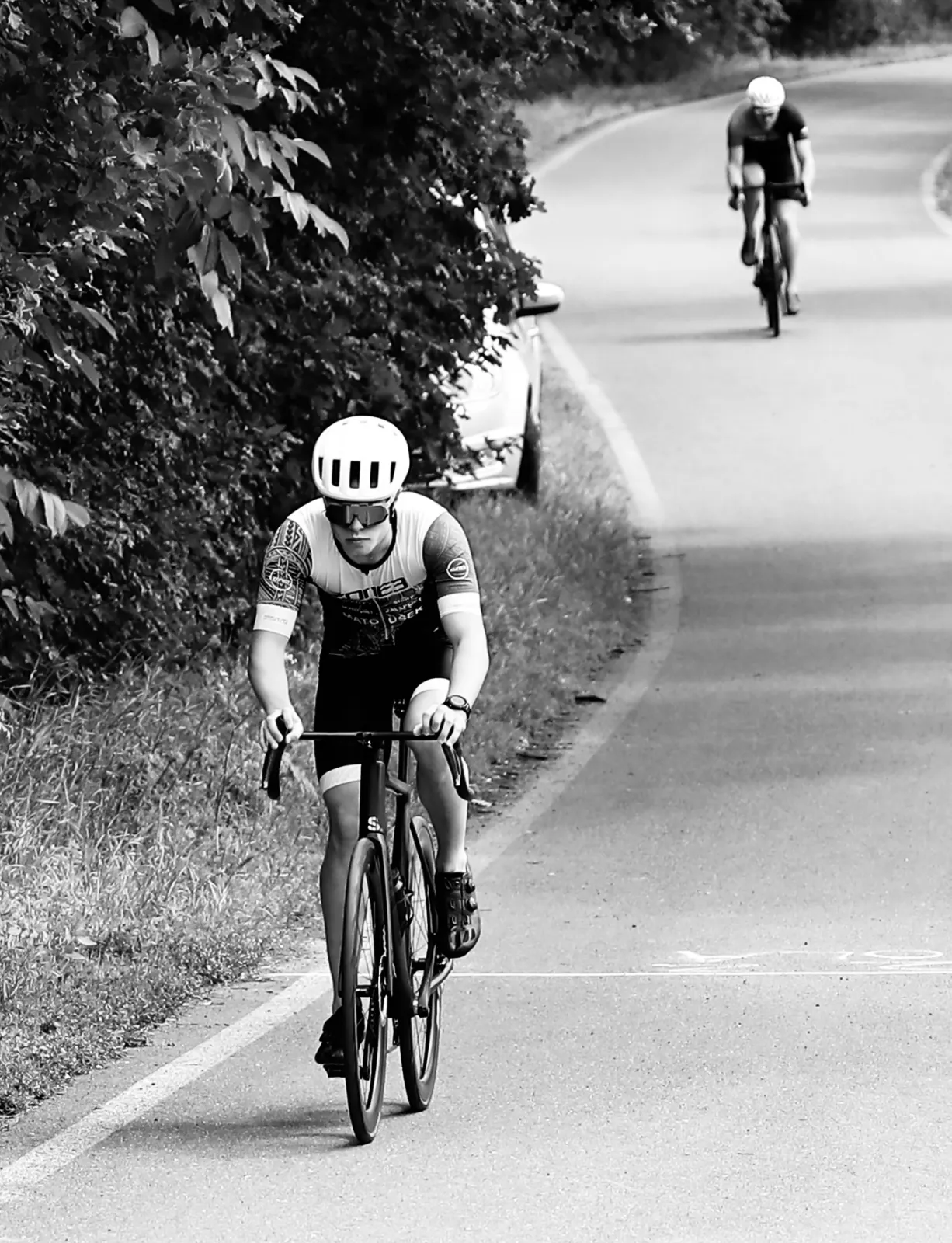 Oliver climbing on a road bike, another rider behind him. Black and white.